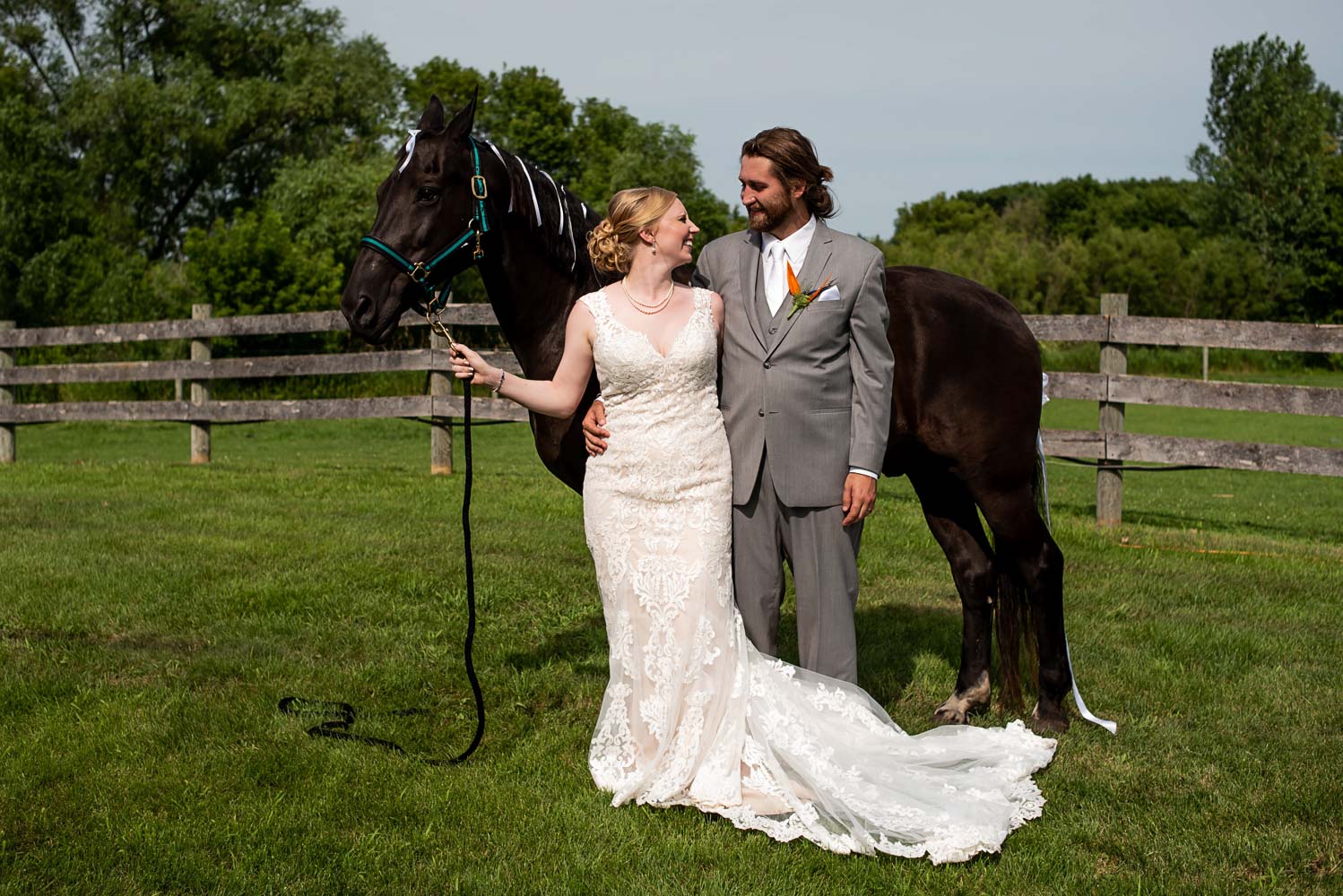 bride and groom standing with a horse on the family farm before their summer wedding