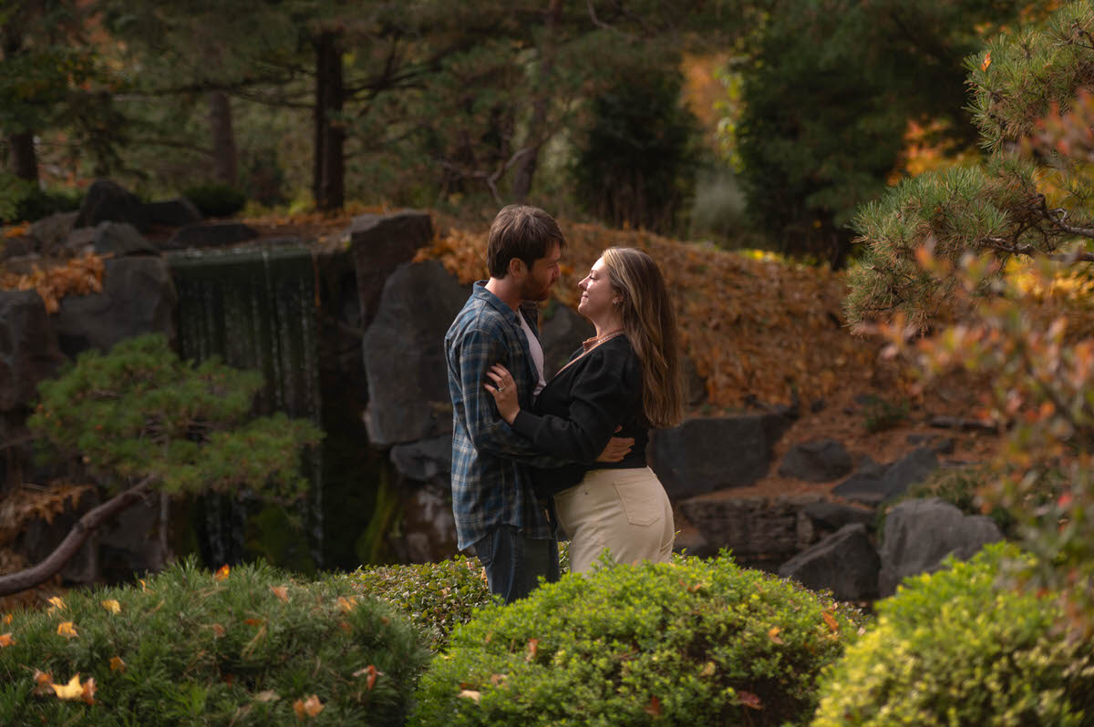 A couple standing in a park with their arms around each other about to kiss