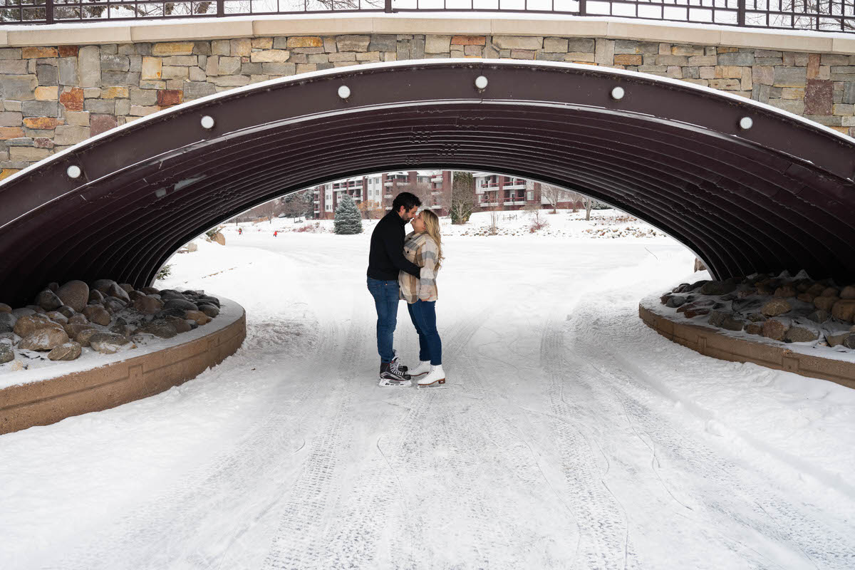A couple about to kiss under a bridge with ice skates on 