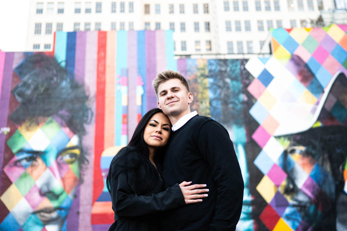 A couple hugging and smiling in front of a colorful mural
