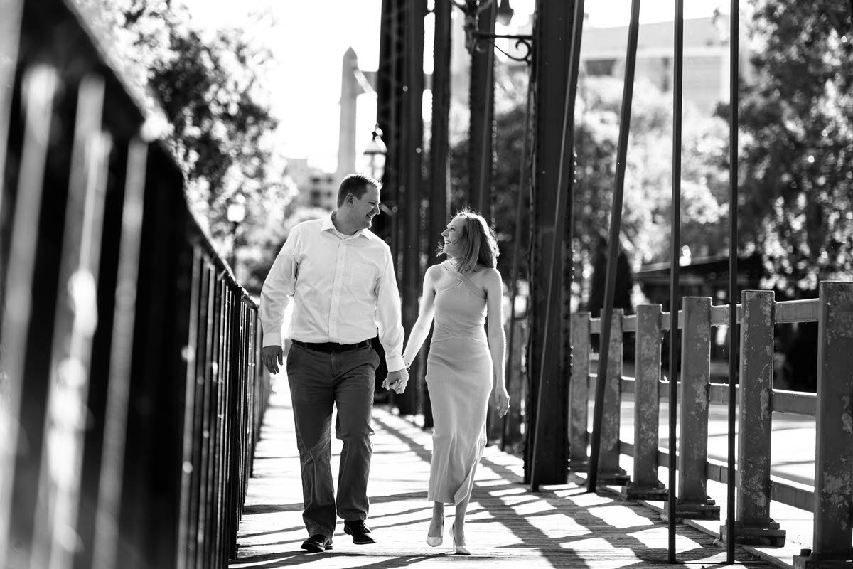 A couple holding hands and smiling as they walk along a bridge