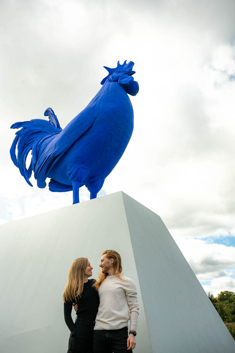 A couple smiling at each other while standing in front of a large blue sculpture 