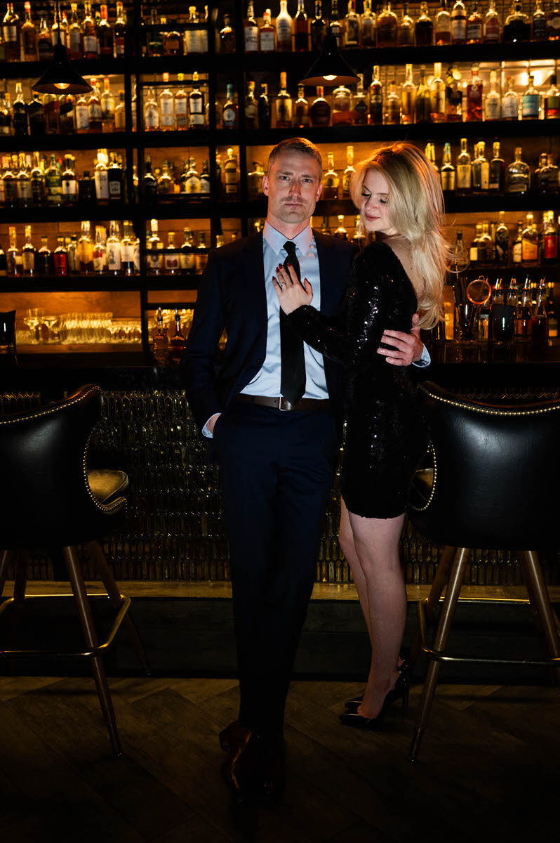 A couple with their arms around each other as they lean on the bar of a speakeasy