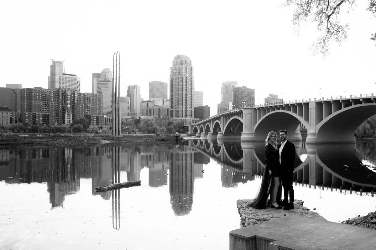 A couple standing together next to a lake with a city skyline behind