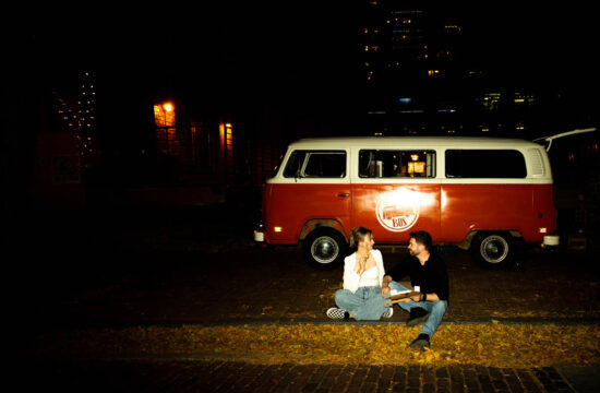 A couple sitting on the ground in front of a retro van