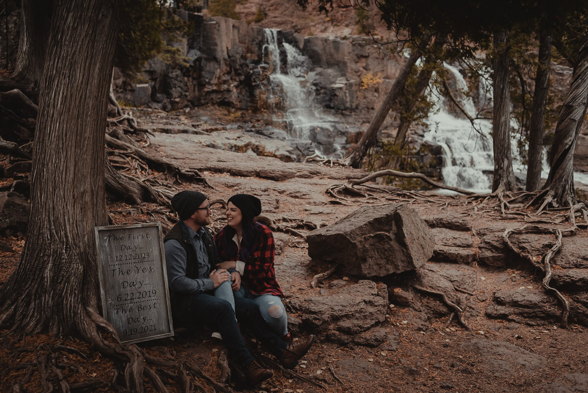 A couple sitting in a wooded area together with a waterfall behind them