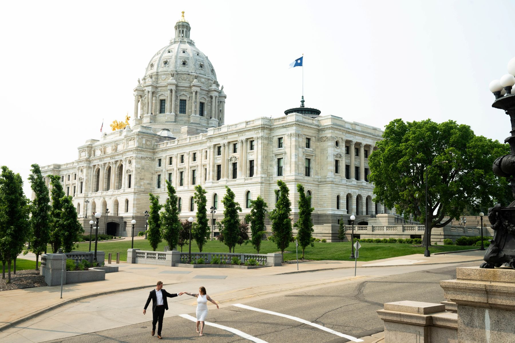a couple taking engagement photos in front of the minnesota state couple holding hands and walking with one another