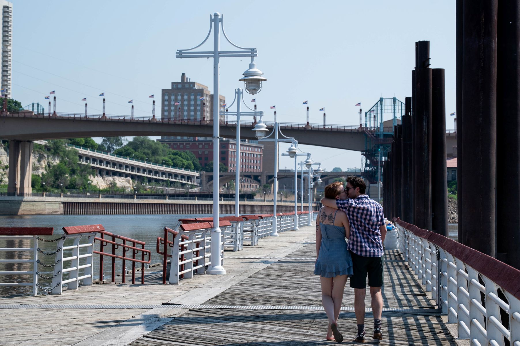 a couple walking down the pavilion at harriet island arm in arm and kissing each other 