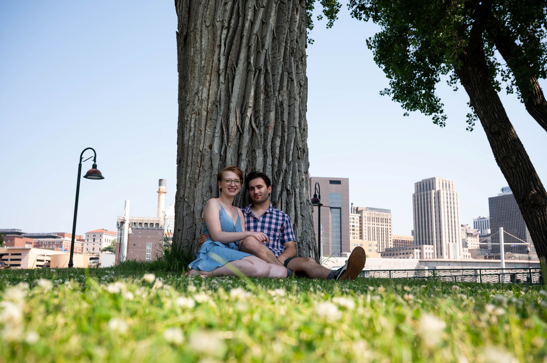 a couple sitting underneath a large tree on a hill on harriet island taking engagement photos