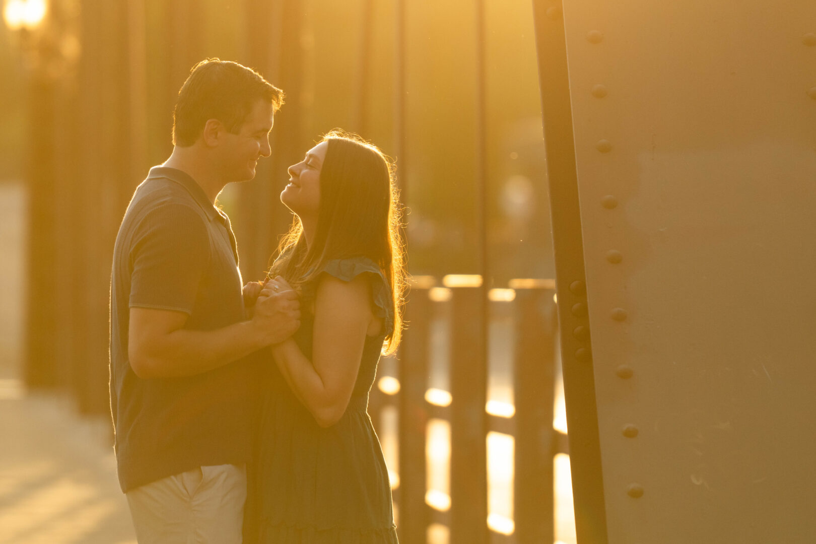 Couple embracing on bridge with beautiful sunset lighting during St. Anthony Main engagement session.