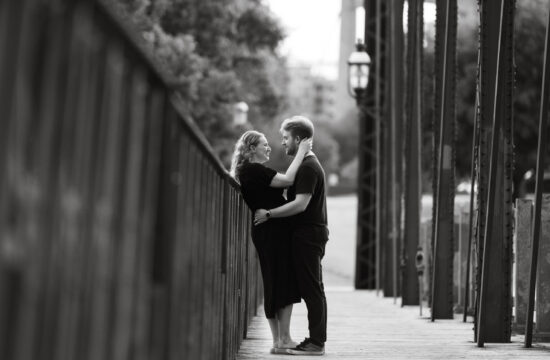 Black and white photo of couple embracing on bridge during St. Anthony Main engagement session.