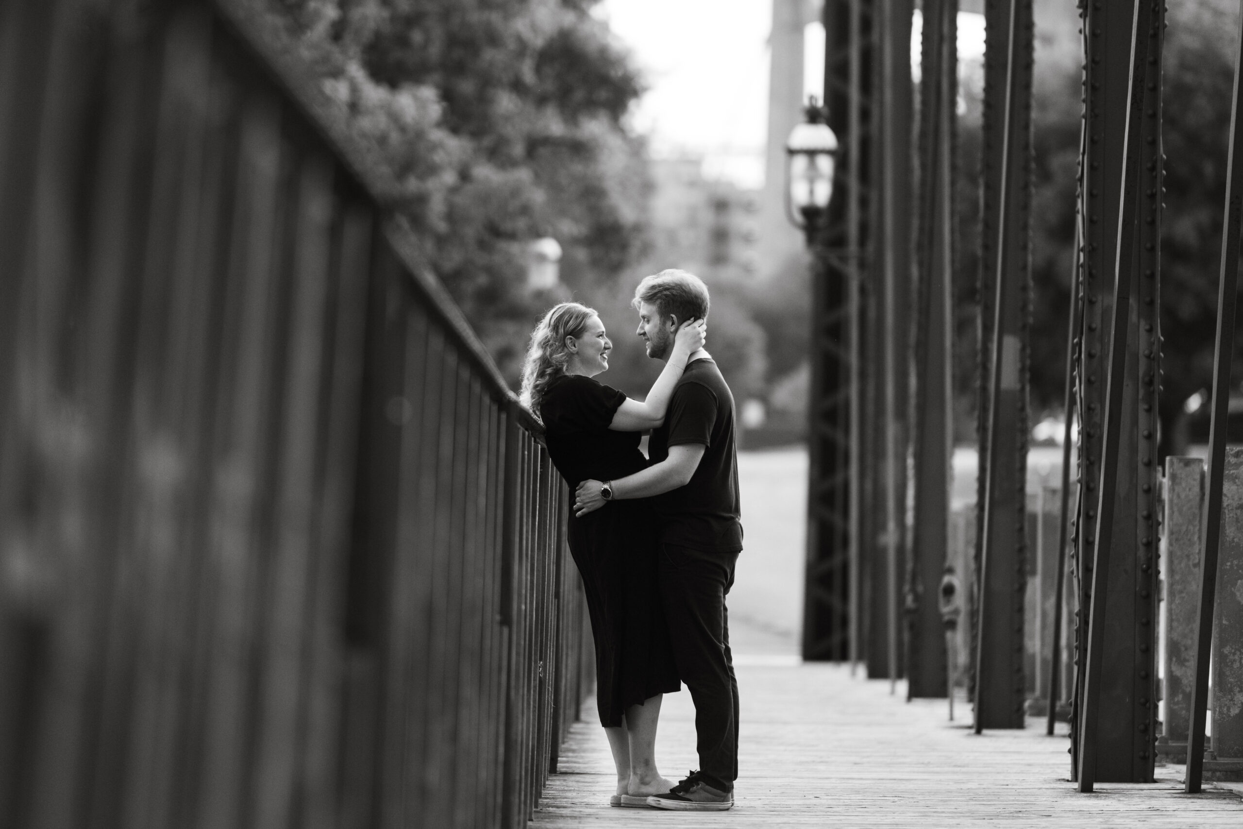 Black and white photo of couple embracing on bridge during St. Anthony Main engagement session.