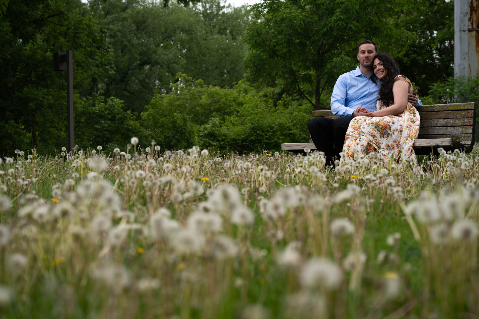 Couple sitting on bench surrounded by beautiful flowers during St. Athony Main engagement session.