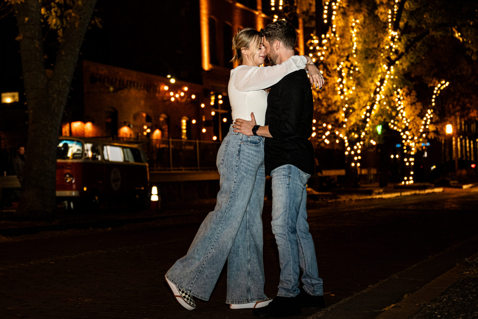 Couple embraces surrounded by evening lights of the city during St. Anthony Main engagement session.