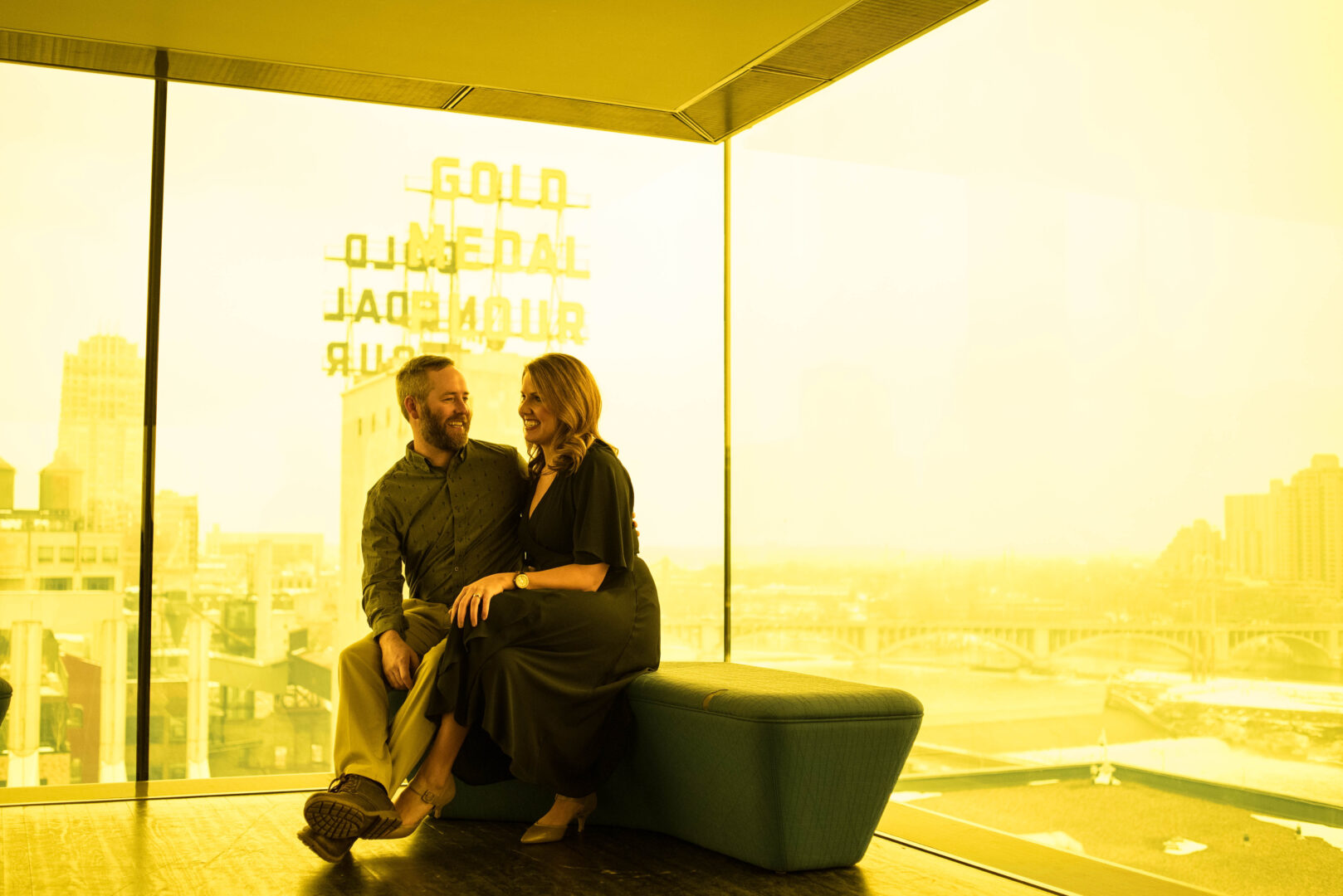 A couple sitting in a room of yellow glass, Minneapolis skyline is out the window at the Guthrie Theater in Minnesota
