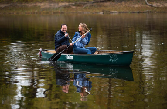 a couple taking engagement photos in a lake they are both sitting in a rowboat together and laughing