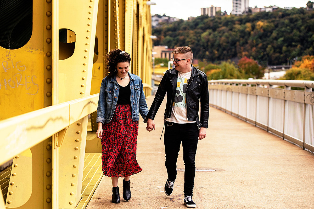 a couple walking hand in hand across a bridge smiling with each other