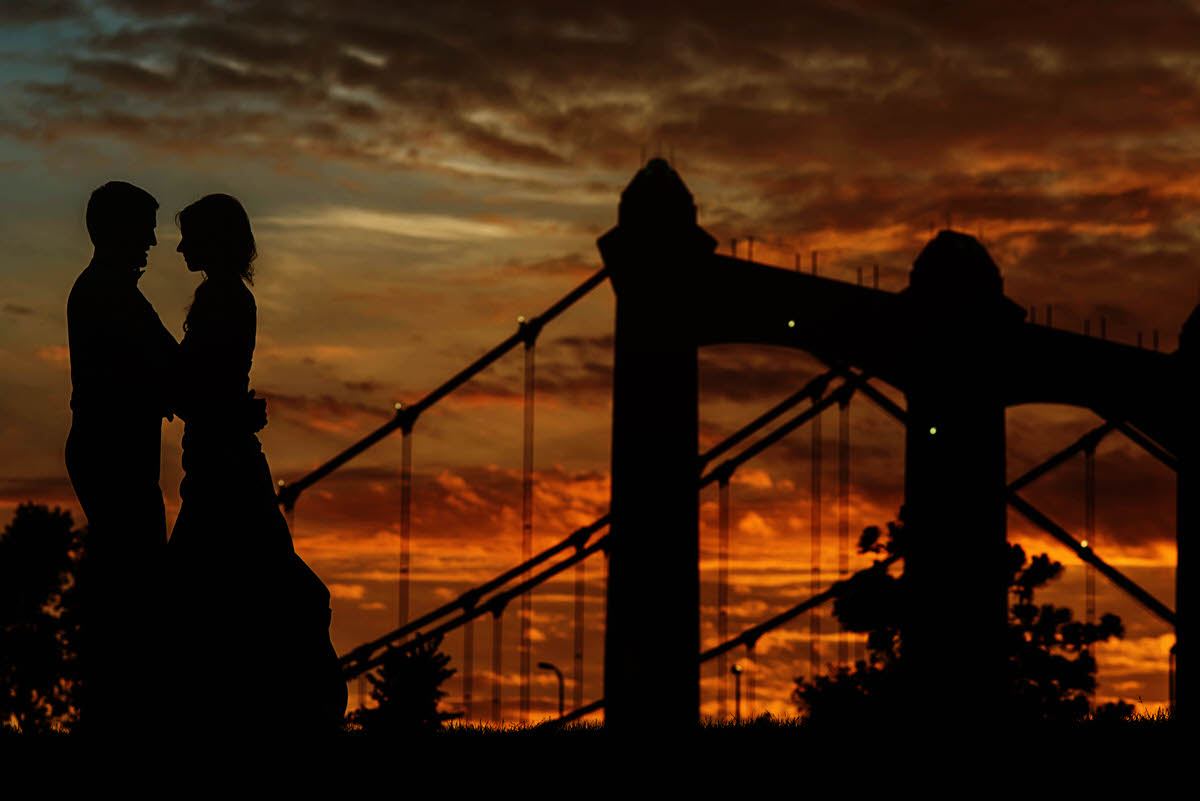 a couple taking golden hour wedding portraits next to a bridge 