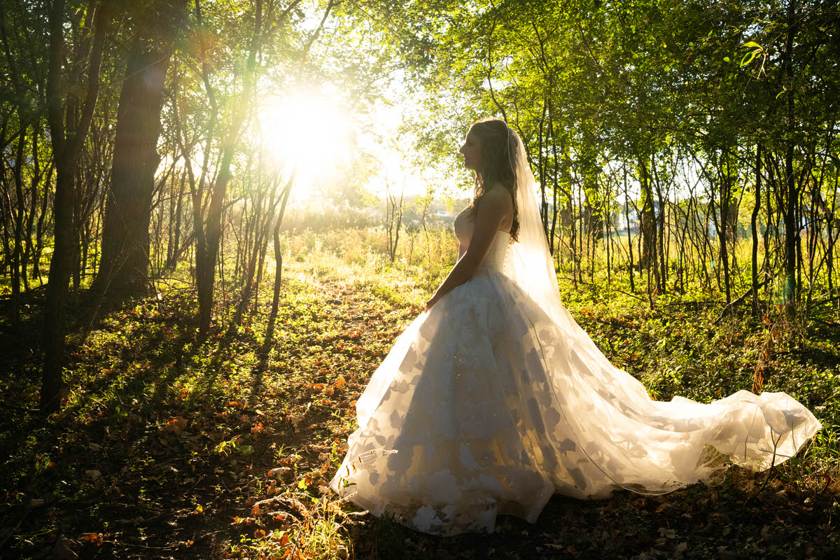 a bride in a white wedding dress and veil taking a golden hour portrait