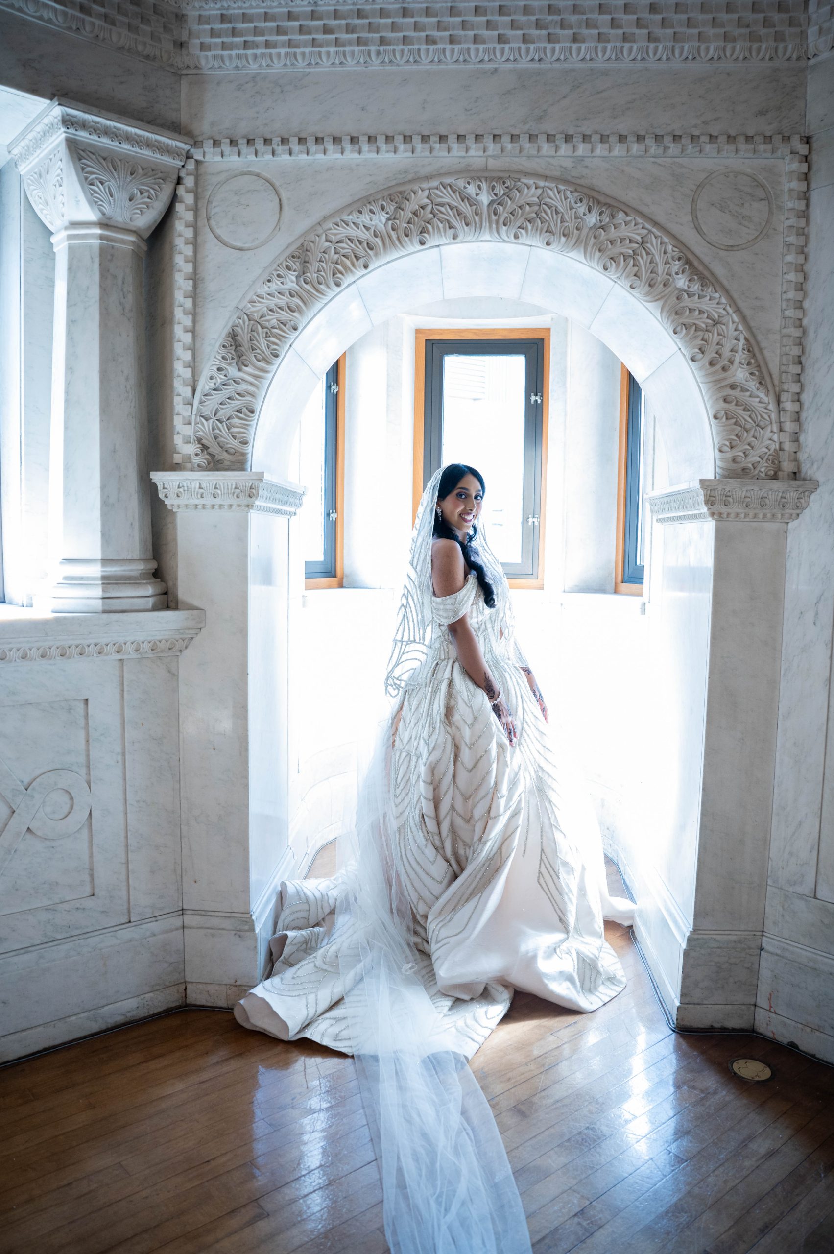a woman in a wedding dress taking photos underneath an arch in the landmark center