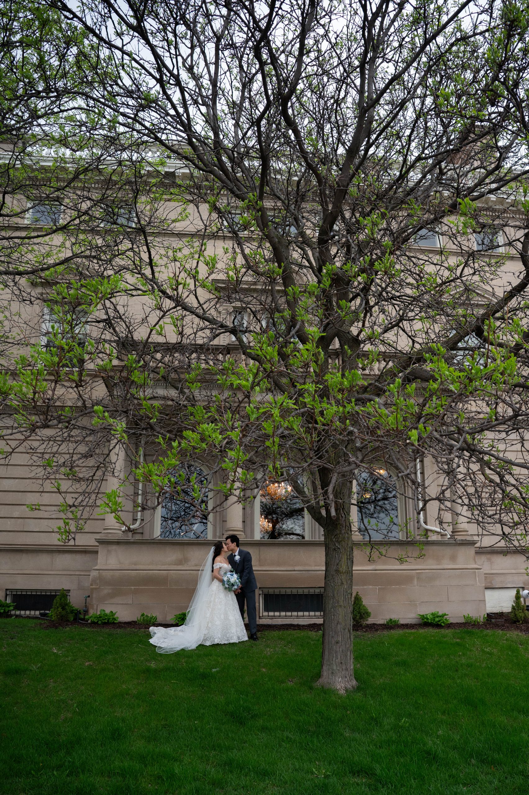a couple in front of the exterior of semple mansion standing underneath a tree taking wedding photos