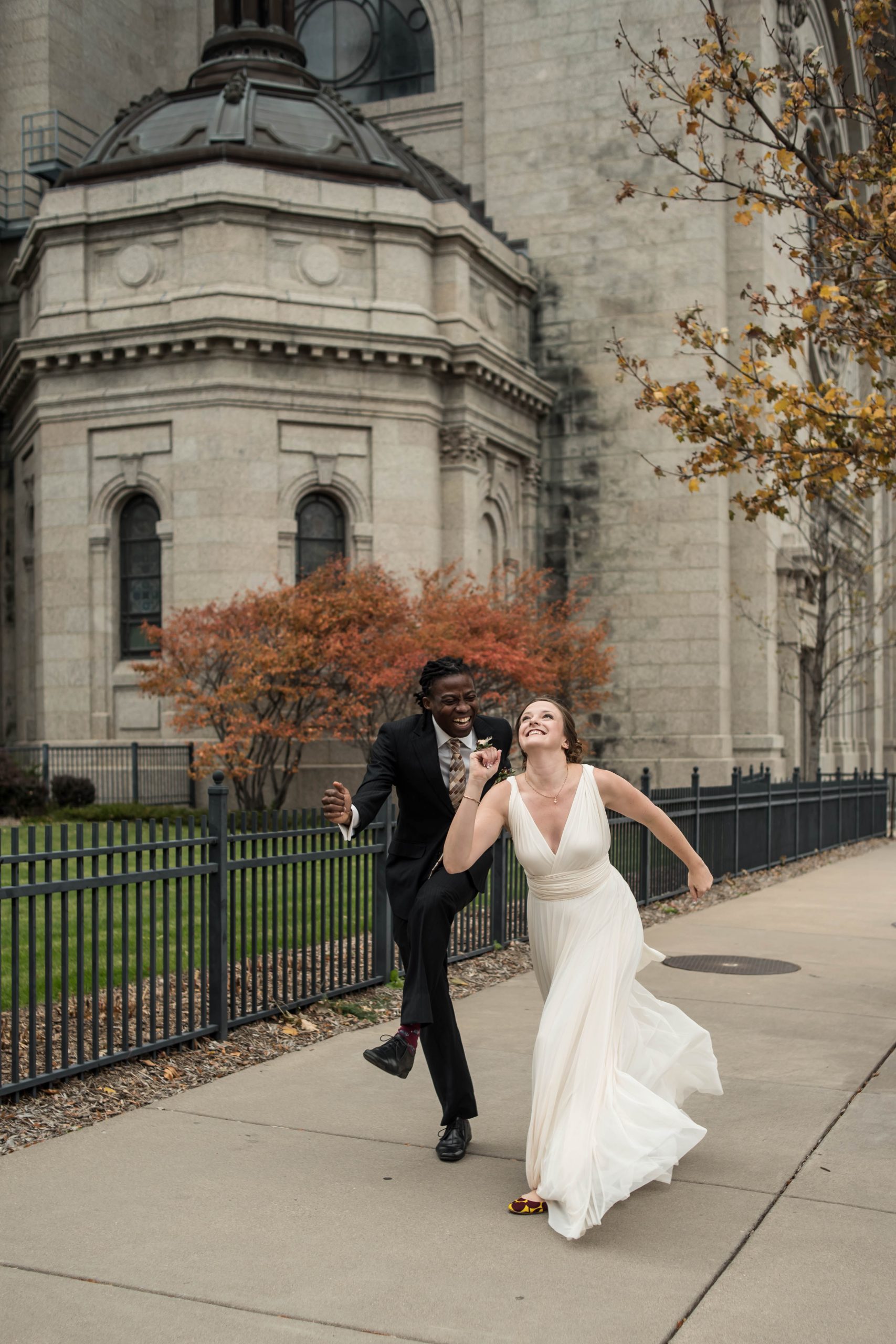 minnesota wedding venues 22 a couple in a wedding dress and suit running down the sidewalk in front of St. Paul's cathedral