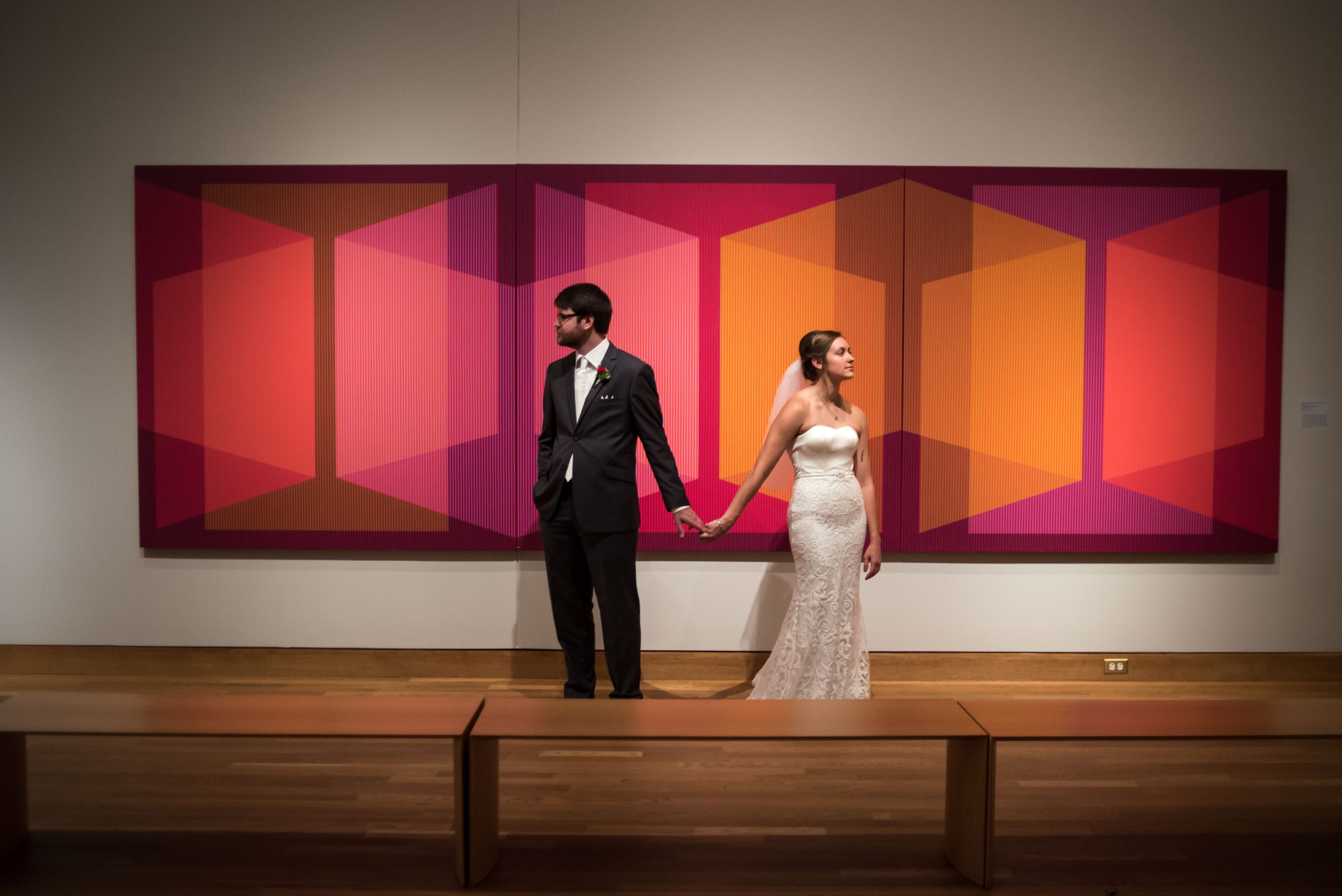 a bride and groom at the Weisman Art Museum taking a wedding portrait in front of a piece of art and holding hands